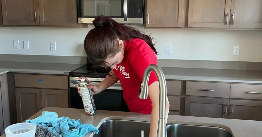 Person cleaning a kitchen countertop with cleaning supplies in hand